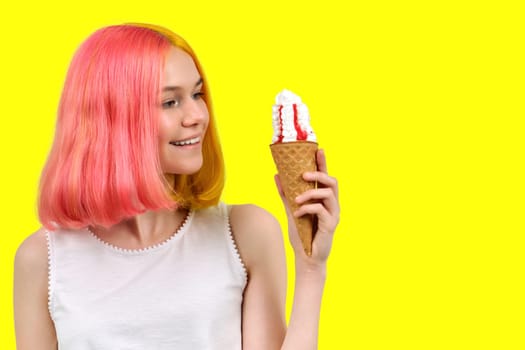 Smiling happy beautiful model teenager with ice cream in waffle cone over yellow studio background. Summer, food, beauty and fashion concept