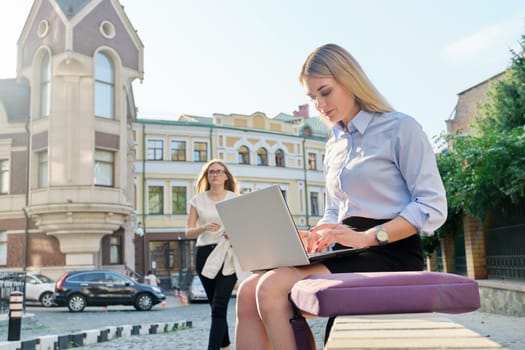 Young businesswoman sitting with laptop looking at the screen, working outdoors. City, freelance, business, lifestyle concept, street business people background