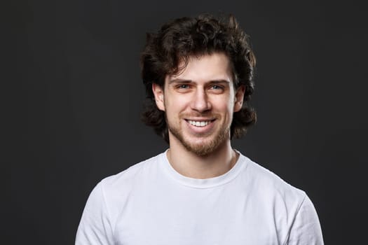 portrait of young smiling curly man on dark gray background