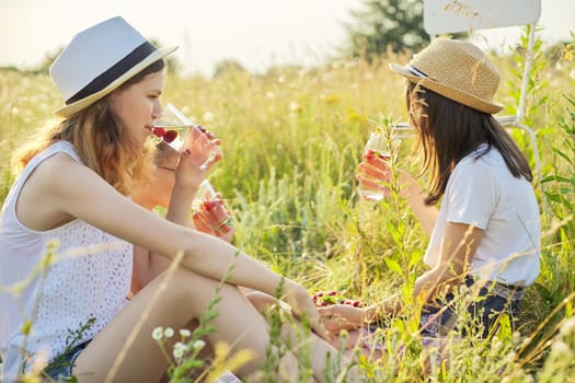 Happy girls kids eating strawberry pie and drinking tea with mint berries on picnic, summer sunny meadow background. Vacation, childhood, fun, summer concept