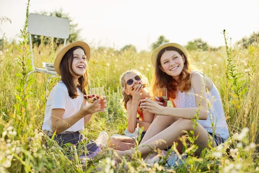 Happy girls kids eating strawberry pie and drinking tea with mint berries on picnic, summer sunny meadow background. Vacation, childhood, fun, summer concept