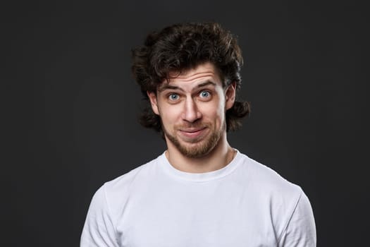 puzzled young bearded man in casual white t-shirt looking at the camera on dark gray background. great idea