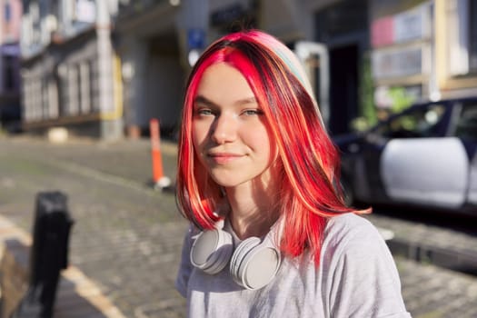 Beautiful smiling happy teenage student with trendy colored hairstyle headphones, street of sunny summer city background