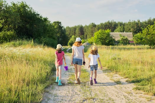 Summer, nature, children. Three girls walking with their backs on a country road, rustic summer landscape background