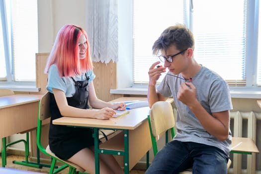 Students teenagers 16 years old in class, boy and girl talking, sitting at a desk at school.