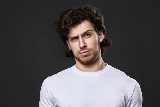 puzzled man in white t-shirt looking suspicious on dark gray background