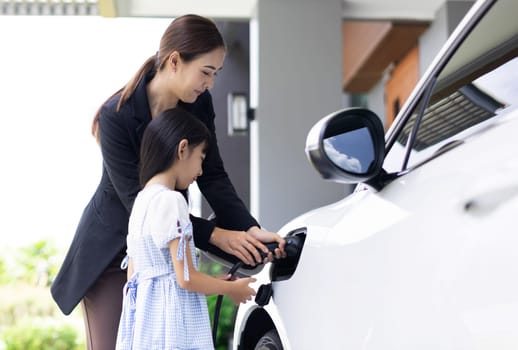 Progressive lifestyle of mother and daughter who have just returned from school in an electric vehicle that is being charged at home. Electric vehicle powered by sustainable clean energy.