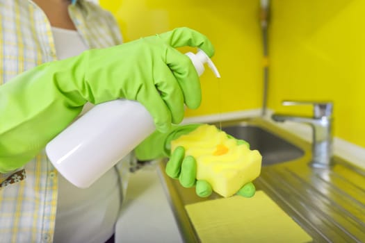 Woman in rubber gloves cleaning kitchen with sponge and bottle of detergent