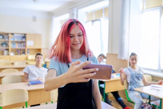 Teenagers students having fun in the classroom, bright trendy girl taking selfie photo with group of classmates friends at school