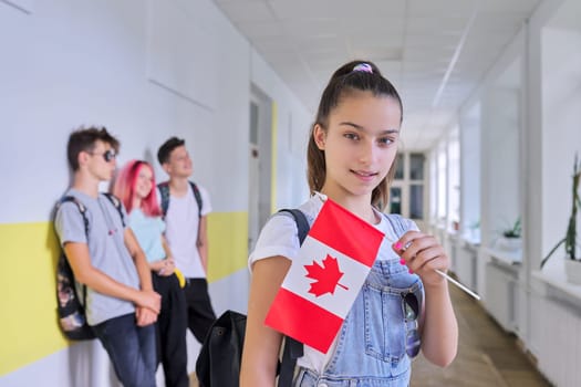 Student teenager female with flag of Canada inside school, children group background. Canada, education and youth, patriotism, people concept