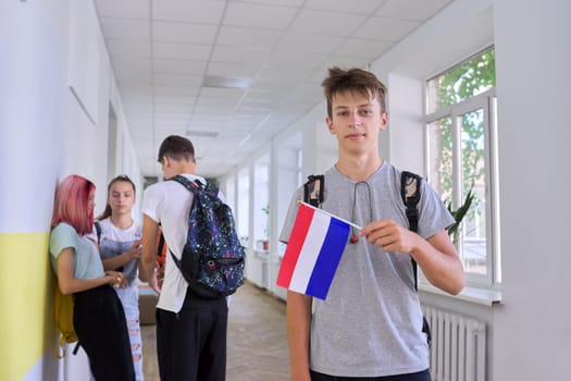 Student teenager male with Netherlands flag inside school, children group background. Europe, Netherlands, education and youth, patriotism people concept