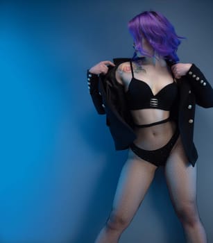 sexy girl in a fancy jacket and purple hair posing erotically in her underwear against a blue background copy paste