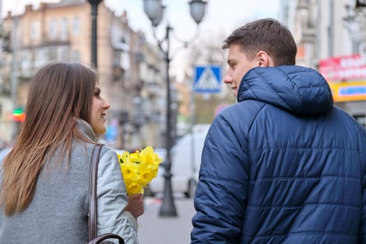 Young couple in love on Valentine's day walking in the city, happy girl with a bouquet of flowers, back view