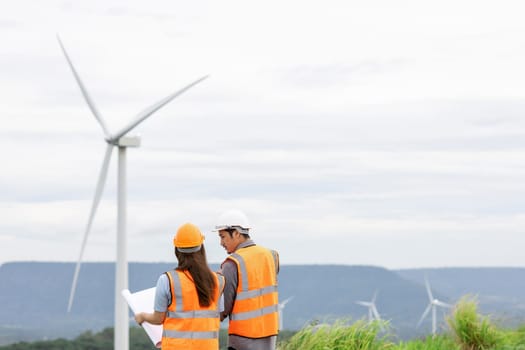 Male and female engineers working on a wind farm atop a hill or mountain in the rural. Progressive ideal for the future production of renewable, sustainable energy.