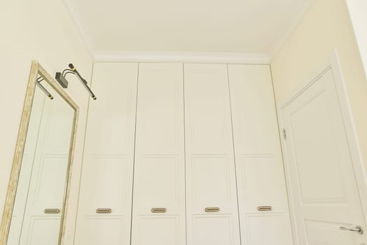 White beige pastel built-in wardrobe in the color of wall. Bedroom interior, with mirror and LED modern lamp above the mirror