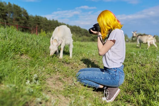 Girl hipster teenager with camera on farm in meadow makes photo of little young goat