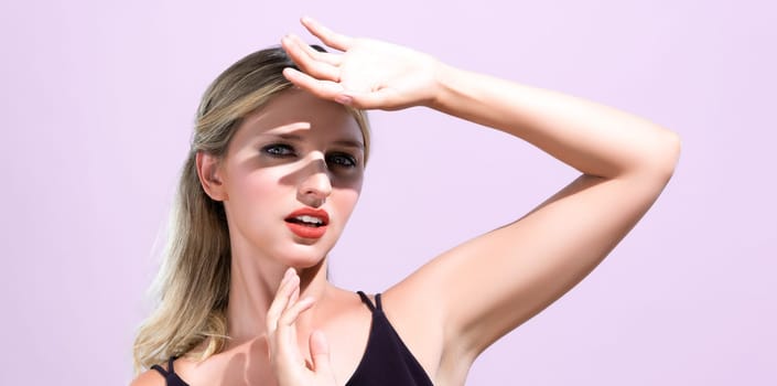 Closeup young blond hair woman with perfect skin and soft alluring facial makeup raise her hand cover her face from bright sunlight in pink isolated background for skincare sunscreen product.