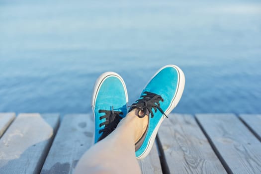 Womans legs in blue sneakers on wooden pier, river lake pond background for copy space. Vacation, nature, lifestyle, people concept