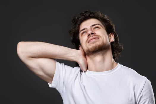 unhappy young man with neck pain on dark gray background