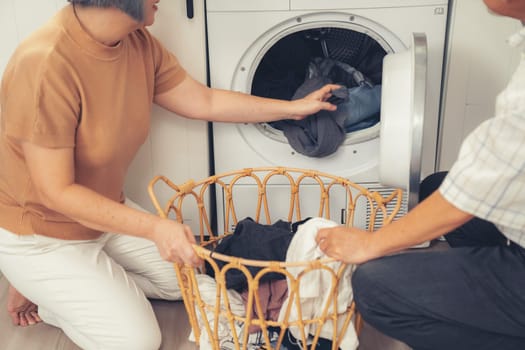 Senior couple working together to complete their household chores at the washing machine in a happy and contented manner. Husband and wife doing the usual tasks in the house.