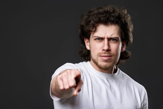 surprised caucasian man pointing finger at you on dark gray background. guy asks a question - is it you