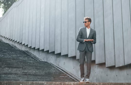 Posing for a camera. Young businessman in grey formal wear is outdoors in the city.