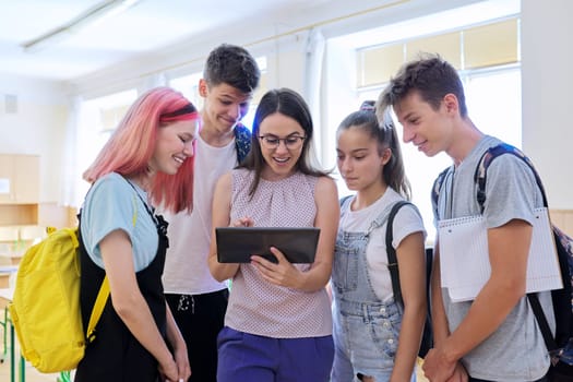 Group of teenage students and young female teacher with digital tablet in classroom, children and tutor looking at computer screen. Education, school, college, schoolchildren concept