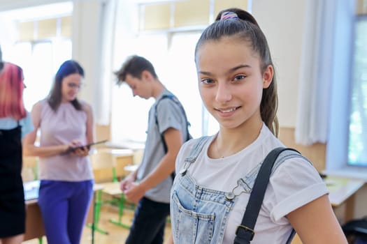 Portrait of teenage looking at camera, student girl in classroom with group of pupils children and female teacher. Education, school, college, teenagers concept