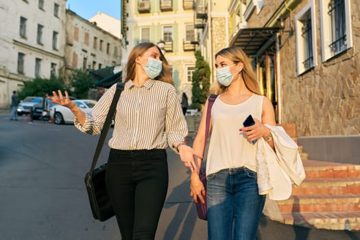 Office workers two young business women walking along the city street wearing medical protective masks. Lifestyle, business in an epidemic, pandemic, bad ecology