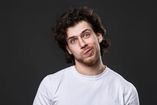 skeptic and nervous man in white t-shirt with disapproving expression on face on dark gray background