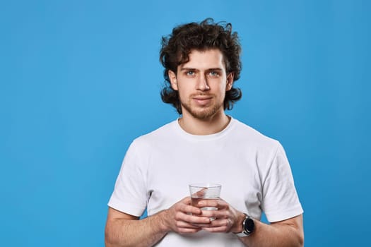 handsome man in white t-shirt holding drinking glass of water on blue background