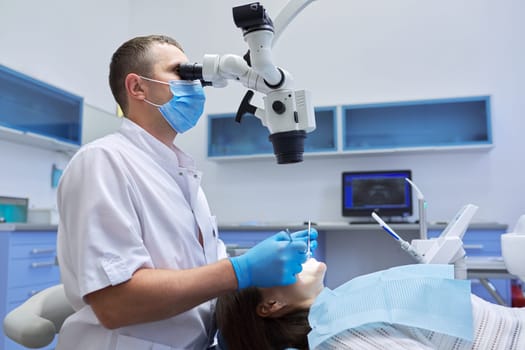 Healthcare dentistry medicine, male doctor dentist treating teeth to a woman patient in chair using dental equipment, tools and microscope, clinic office interior background