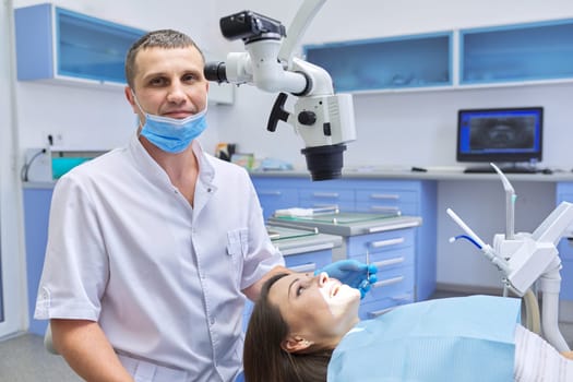 Healthcare dentistry medicine, male doctor dentist treating teeth to a woman patient in chair using dental equipment, tools and microscope, clinic office interior background