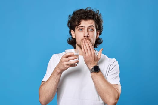 Young surprised handsome man with drinking glass of water on blue background