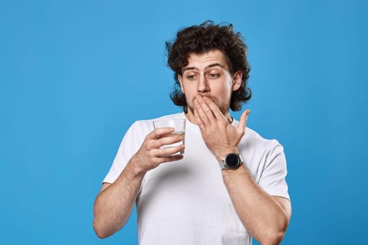 Young surprised handsome man with drinking glass of water on blue background