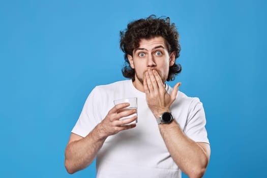 Young surprised handsome man with drinking glass of water on blue background