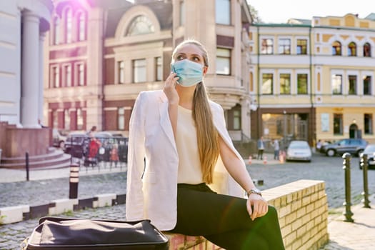 Young business woman in medical protective mask talking on smartphone outdoors, city street background. Business, pandemic, epidemic, healthcare and medicine, healthy lifestyle
