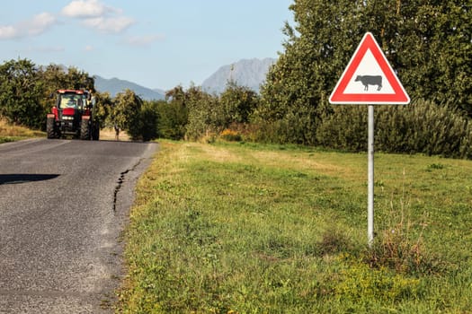 Liptovsky Hradok, Slovakia - August 22nd, 2018: Caution cows crossing sign, next to road with tractor coming, countryside, hills and mountains in distance.