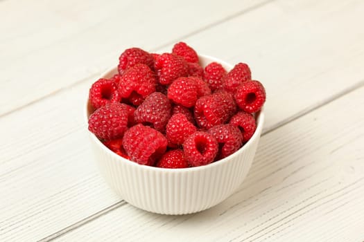 Small porcelain cup with raspberries on white boards desk.