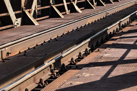 Detail of railway tracks on old metal bridge, sun casting shadows on them.