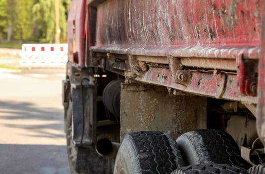 Closeup of old rusty and dirty truck side,  paint peeling on cargo area wall, large tires visible, blurred road block sign id distance. Roadworks illustration.