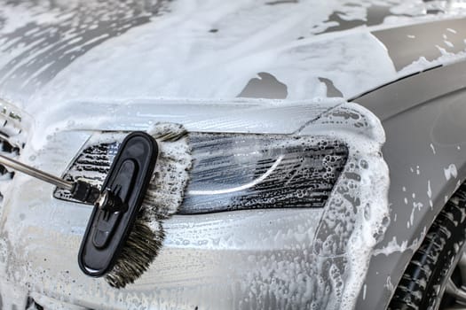 Car cleaned at manual carwash brush leaving strokes in shampoo on front light glass.