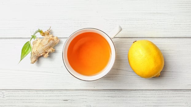 Table top view, cup of freshly brewed tea, lemon, and dry ginger root with green sprout, next to it.