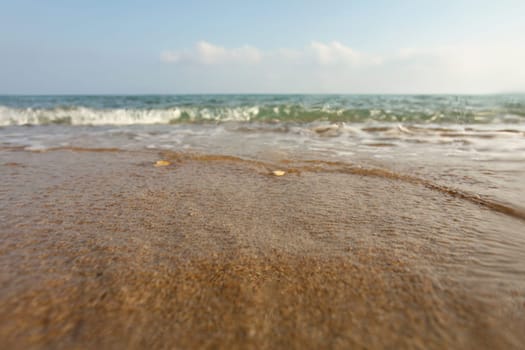 Wet sand on the beach, sea in distance, low angle photo on ground level, lens covered with some drops to emphasise water. Abstract marine background.