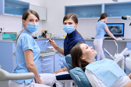 Dental examination, treatment of teeth, patient mature woman in chair and doctor dentist with an assistant. Medicine, dentistry and health care concept