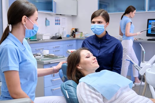 Dental examination, treatment of teeth, patient mature woman in chair and doctor dentist with an assistant. Medicine, dentistry and health care concept