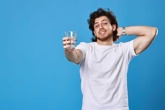 Young smiling handsome man offering a glass of water on blue background. focus on glass. copy space