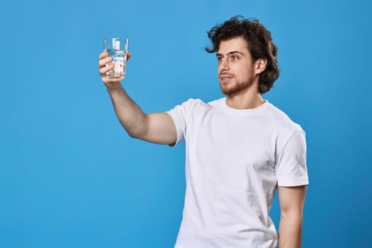 Young handsome man with drinking glass of water smiling happy on blue background
