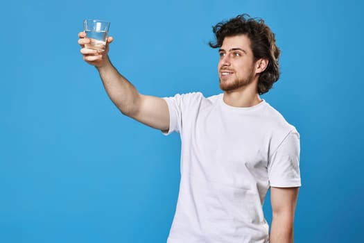 Young handsome man with drinking glass of water smiling happy on blue background