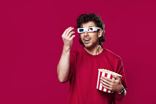 handsome bearded man in 3d-glasses, t-shirt showing popcorn on magenta background